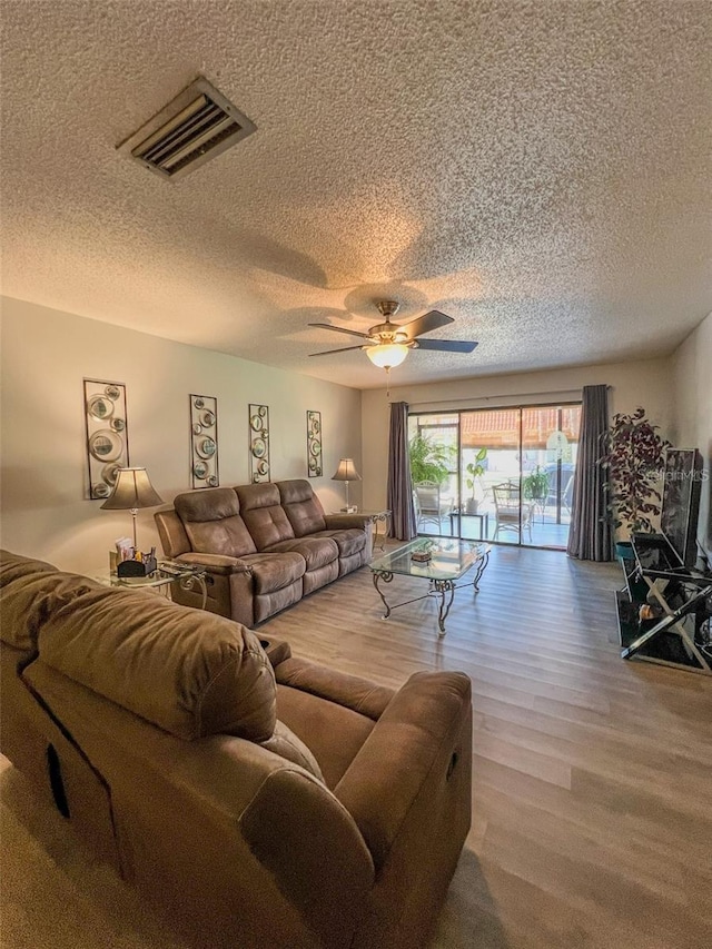 living room featuring a textured ceiling, wood finished floors, visible vents, and a ceiling fan