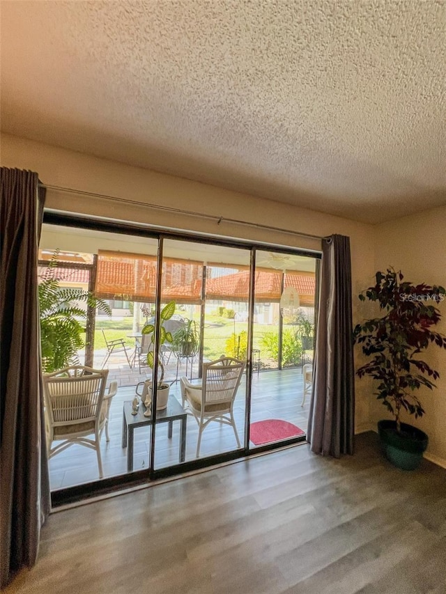 doorway to outside with a textured ceiling and wood finished floors