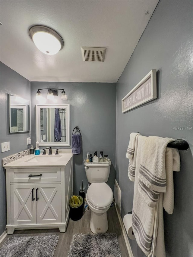 bathroom featuring toilet, wood finished floors, vanity, visible vents, and baseboards