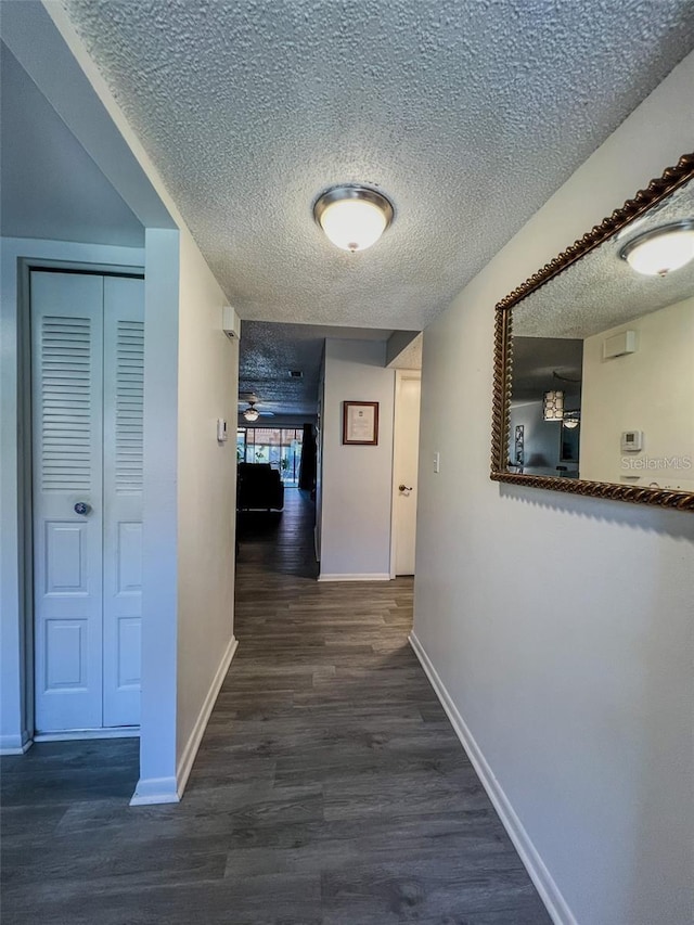 hallway with a textured ceiling, baseboards, and wood finished floors