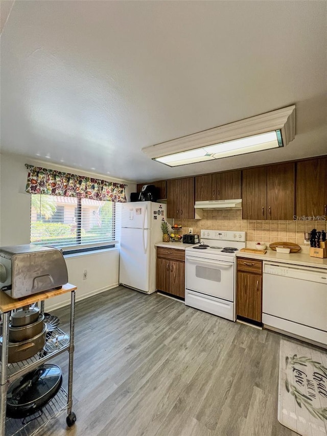 kitchen with white appliances, tasteful backsplash, under cabinet range hood, and light countertops