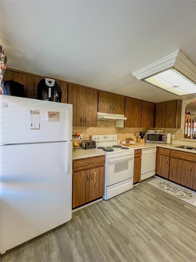 kitchen featuring white appliances, tasteful backsplash, light wood-style flooring, light countertops, and under cabinet range hood