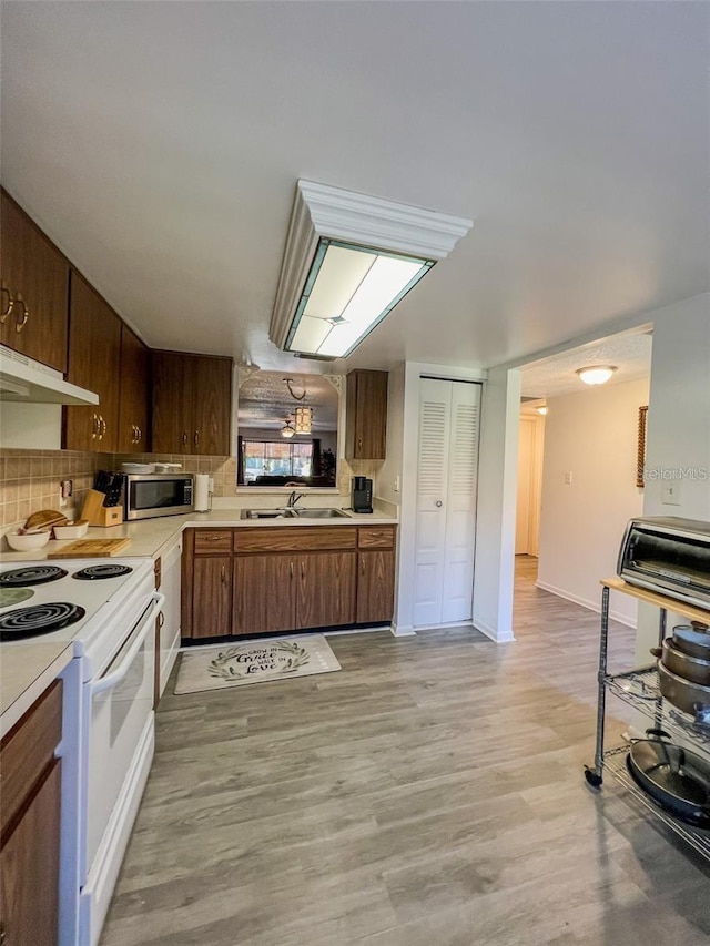 kitchen with white range with electric stovetop, stainless steel microwave, light countertops, under cabinet range hood, and a sink