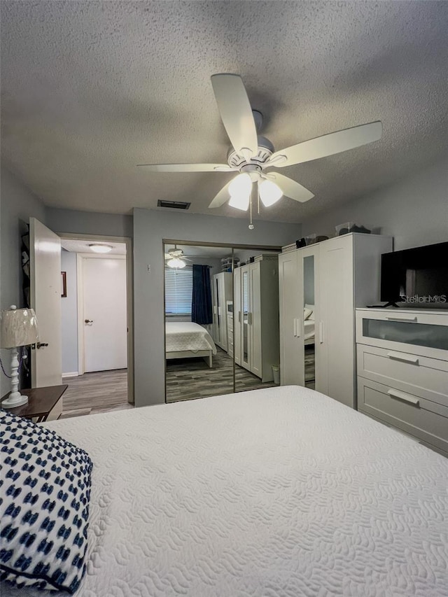 bedroom featuring a barn door, visible vents, a ceiling fan, wood finished floors, and a textured ceiling