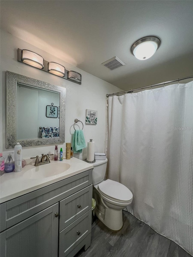 bathroom featuring toilet, vanity, wood finished floors, and visible vents