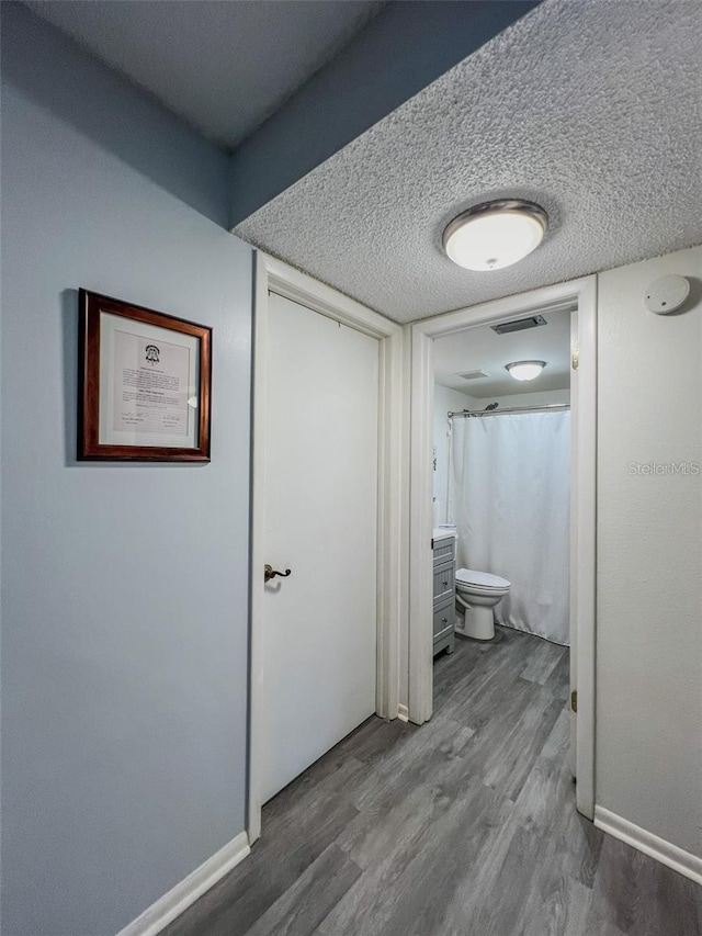 hall with baseboards, visible vents, a textured ceiling, and wood finished floors