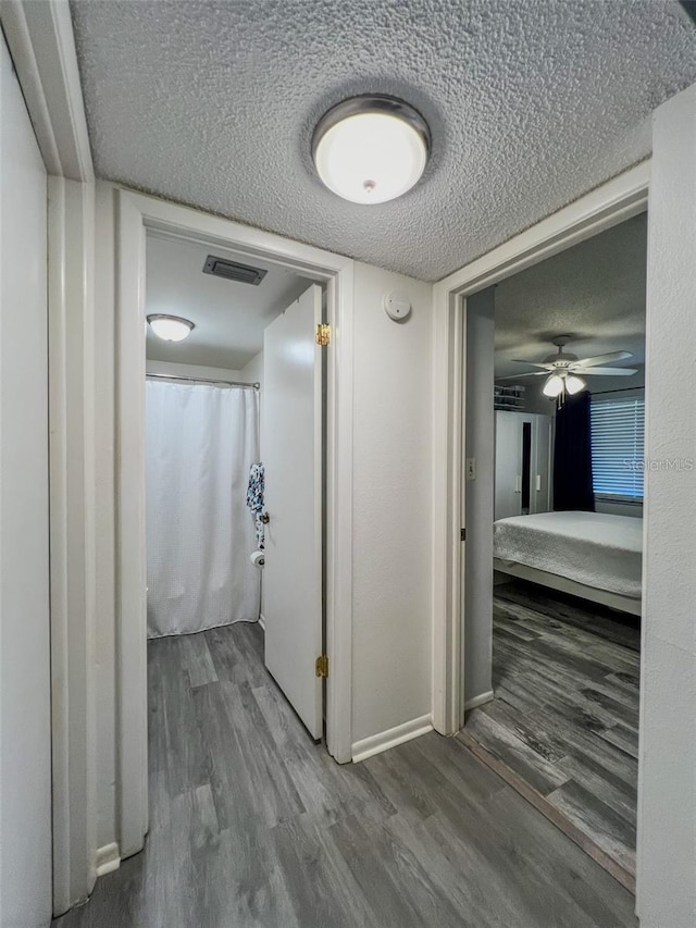 corridor with baseboards, visible vents, a textured ceiling, and wood finished floors