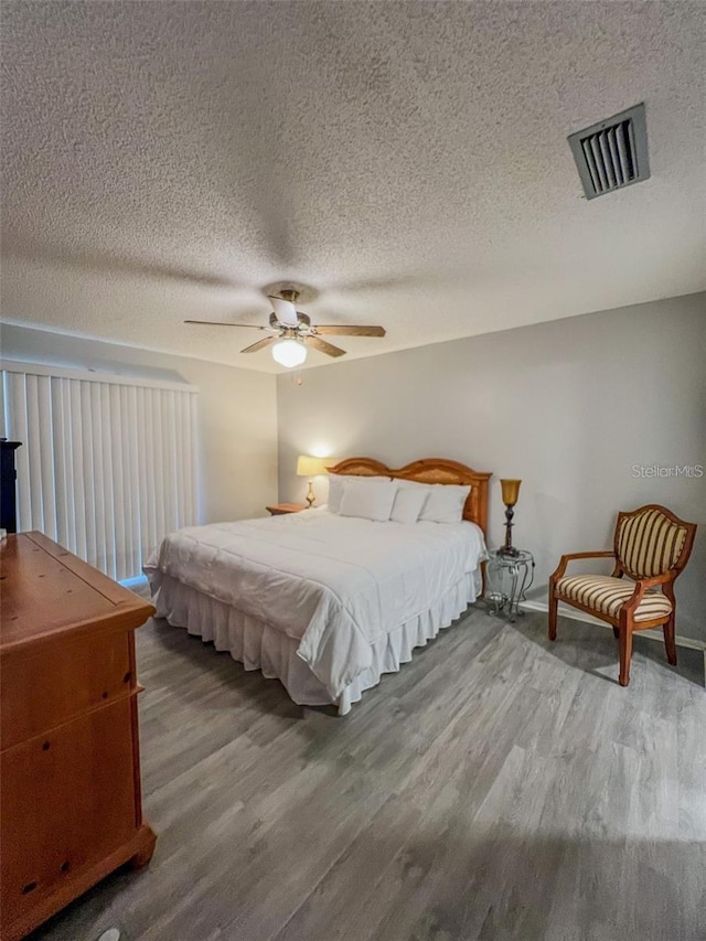 bedroom with a ceiling fan, visible vents, a textured ceiling, and wood finished floors