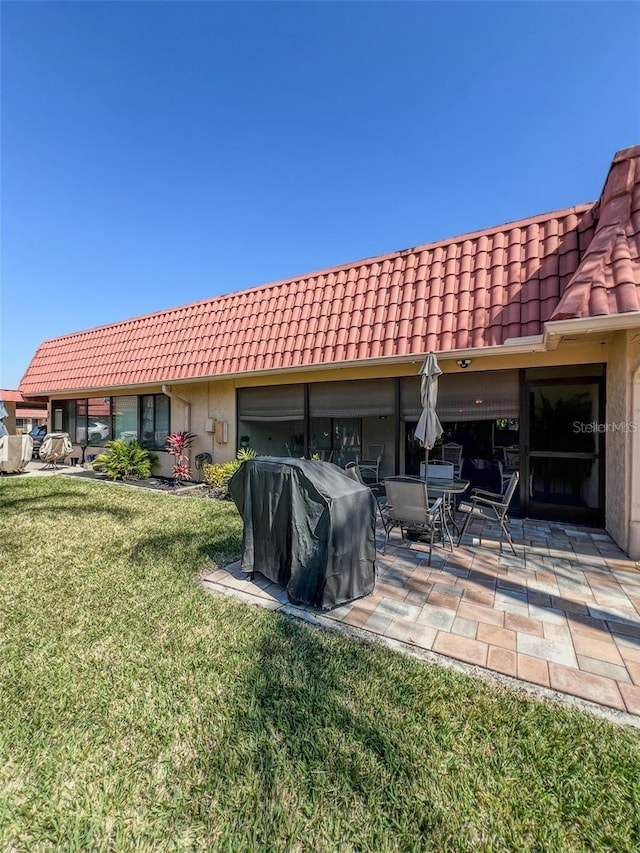 rear view of house with a patio, a lawn, a tile roof, and stucco siding