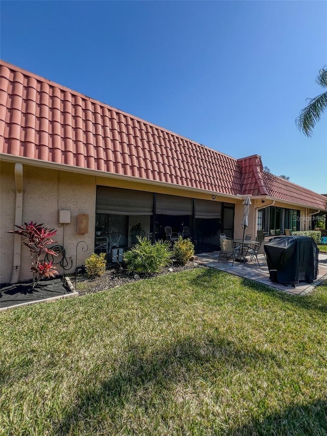 rear view of property featuring a patio, a lawn, a tile roof, and stucco siding