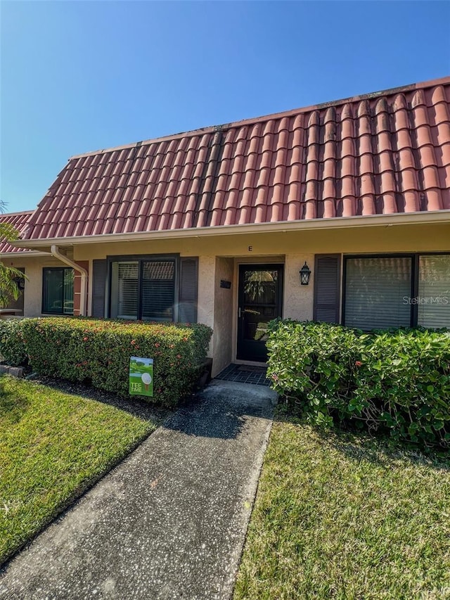 multi unit property featuring a tiled roof, a front lawn, and stucco siding