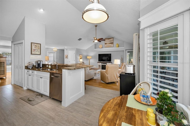 kitchen featuring dark stone counters, lofted ceiling, ceiling fan, white cabinetry, and stainless steel dishwasher