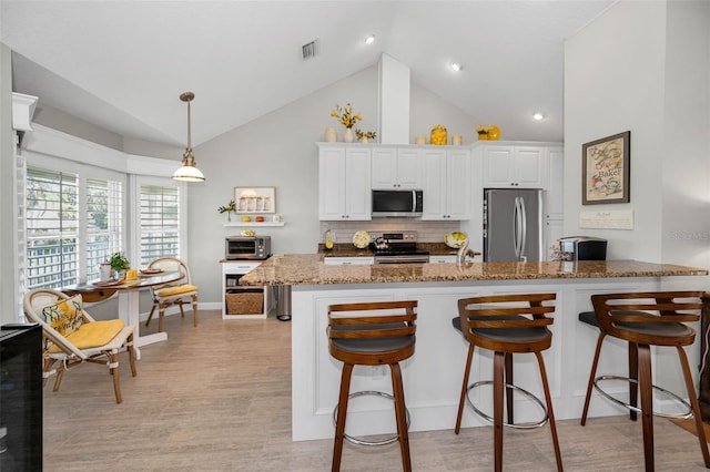 kitchen with appliances with stainless steel finishes, stone counters, a kitchen bar, and white cabinets