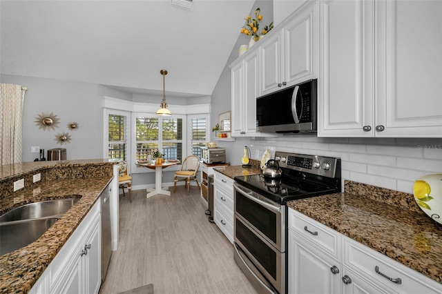 kitchen featuring lofted ceiling, white cabinets, appliances with stainless steel finishes, dark stone counters, and tasteful backsplash