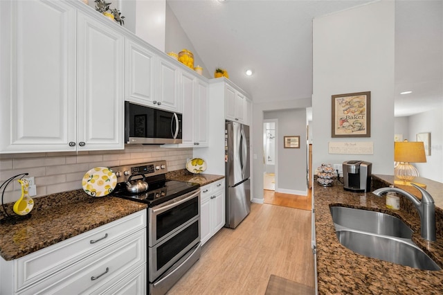 kitchen featuring white cabinets, lofted ceiling, light wood-style flooring, stainless steel appliances, and a sink