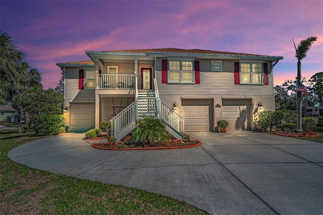 raised beach house with driveway, an attached garage, stairway, and a porch