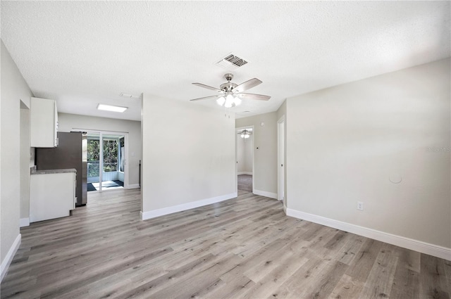 empty room featuring light wood-style floors, baseboards, visible vents, and a textured ceiling