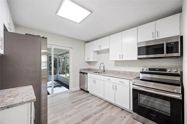 kitchen featuring a textured ceiling, stainless steel appliances, a sink, white cabinetry, and light wood-style floors