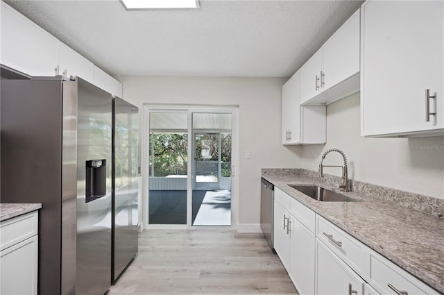 kitchen featuring light wood finished floors, appliances with stainless steel finishes, white cabinets, a sink, and light stone countertops