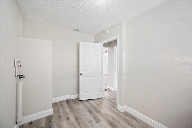 unfurnished bedroom featuring visible vents, a textured ceiling, baseboards, and wood finished floors