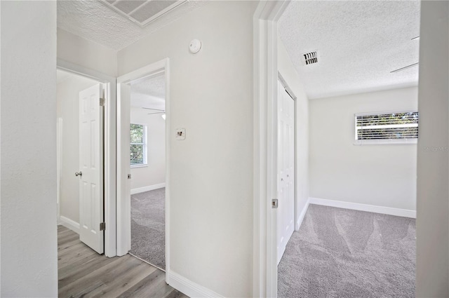 hallway featuring a textured ceiling, carpet floors, visible vents, and baseboards