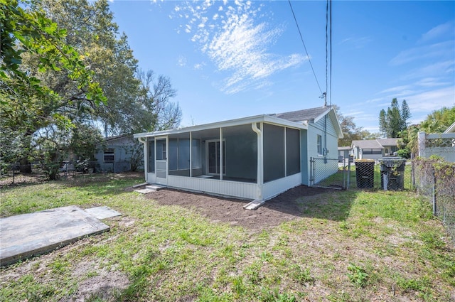 rear view of property featuring a sunroom, a lawn, fence, and a gate