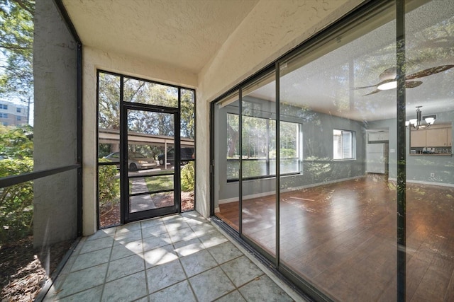 unfurnished sunroom featuring ceiling fan with notable chandelier