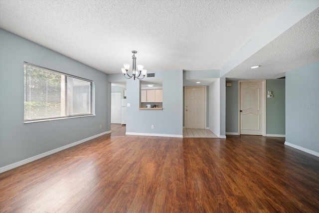 unfurnished living room with baseboards, a notable chandelier, wood finished floors, and a textured ceiling