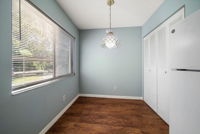 unfurnished dining area featuring a textured ceiling, baseboards, and wood finished floors