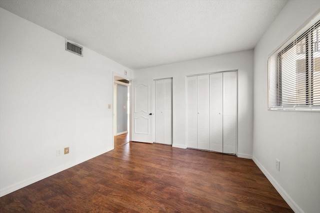 unfurnished bedroom with wood finished floors, baseboards, visible vents, multiple closets, and a textured ceiling