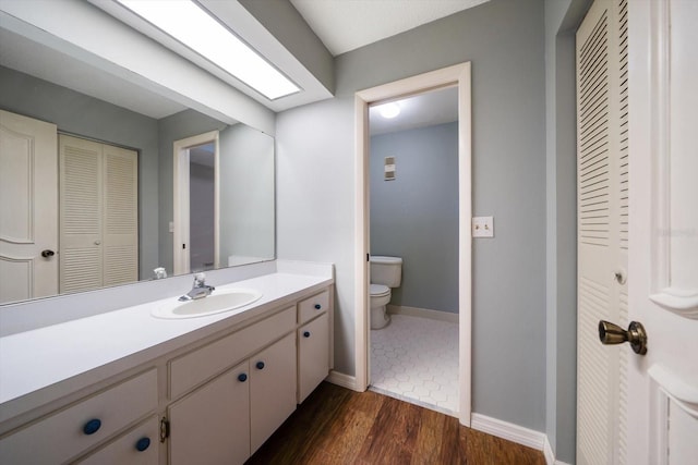 bathroom featuring baseboards, toilet, wood finished floors, a closet, and vanity