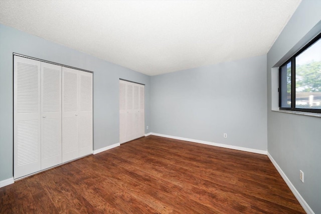 unfurnished bedroom with wood finished floors, baseboards, and two closets