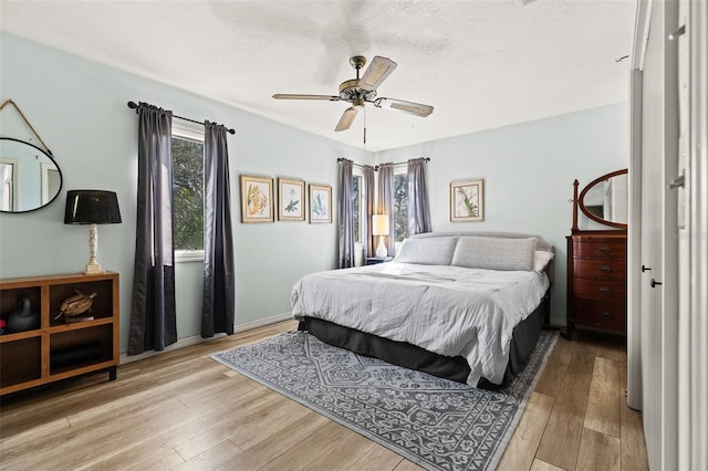 bedroom with a textured ceiling, wood finished floors, a ceiling fan, and baseboards