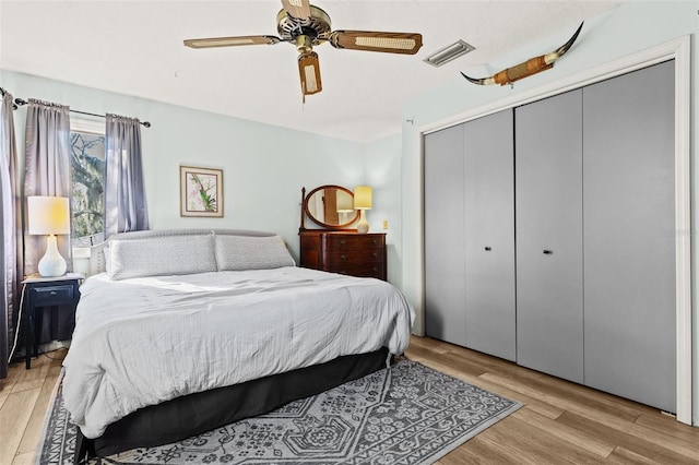 bedroom with light wood-style floors, a ceiling fan, visible vents, and a closet