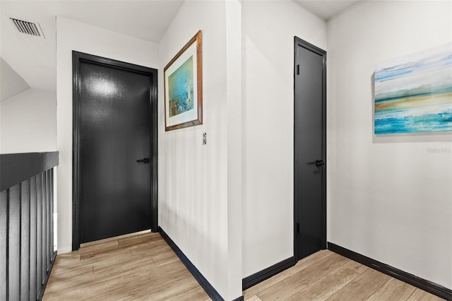 hall featuring light wood-style flooring, visible vents, and baseboards