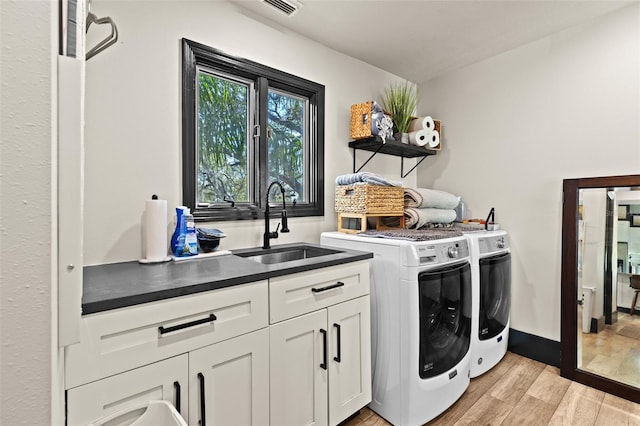 laundry room featuring washing machine and dryer, a sink, visible vents, light wood-style floors, and cabinet space