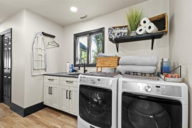 laundry area featuring light wood-style flooring, a sink, visible vents, cabinet space, and washing machine and clothes dryer