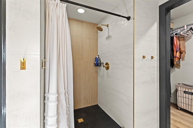 bathroom with wood finished floors, a tile shower, and a walk in closet