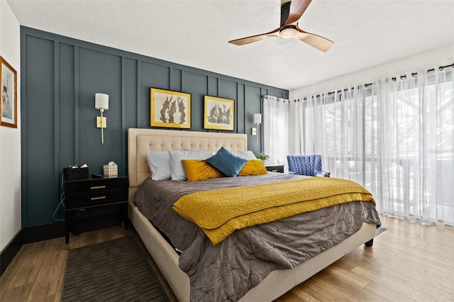 bedroom featuring ceiling fan, a textured ceiling, wood finished floors, and a decorative wall