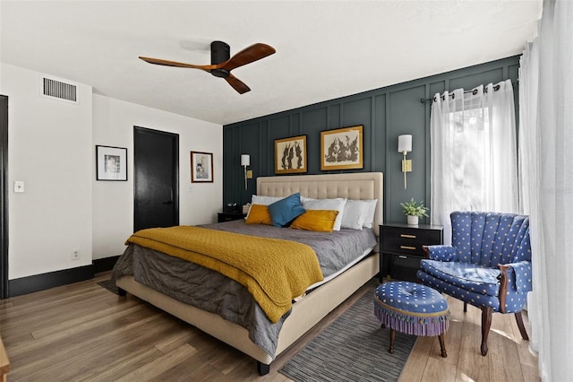 bedroom with a ceiling fan, visible vents, a decorative wall, and wood finished floors