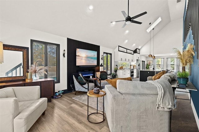 living area featuring ceiling fan, high vaulted ceiling, wood finished floors, and a healthy amount of sunlight