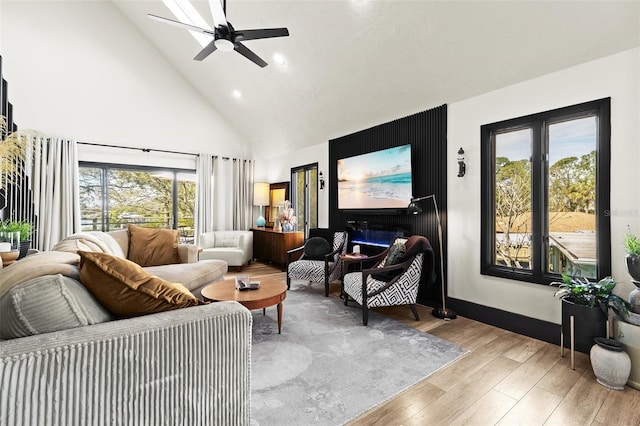 living area featuring light wood-style floors, ceiling fan, high vaulted ceiling, and baseboards