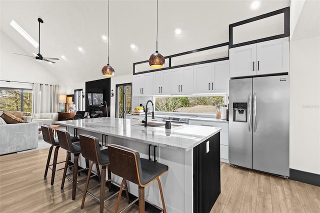 kitchen with light stone counters, a center island with sink, light wood-style floors, white cabinets, and stainless steel fridge with ice dispenser