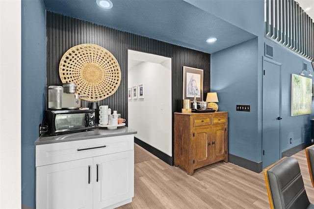 bar with visible vents, a textured ceiling, light wood-type flooring, black microwave, and baseboards