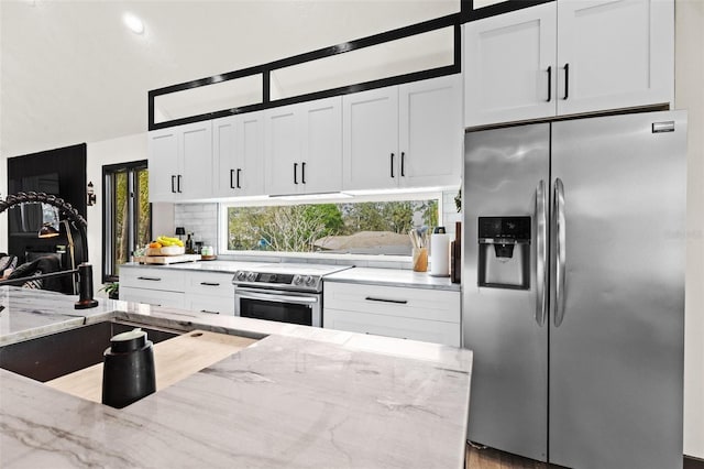 kitchen with appliances with stainless steel finishes, white cabinetry, a sink, and light stone counters