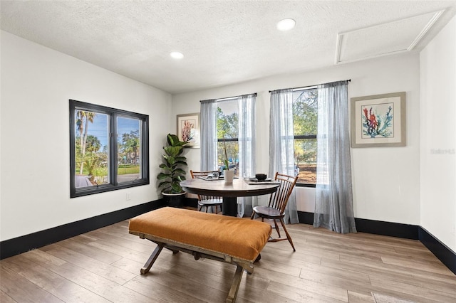 dining room with light wood-style floors, attic access, baseboards, and a textured ceiling