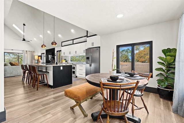 dining space with light wood-style floors, ceiling fan, a textured ceiling, and high vaulted ceiling