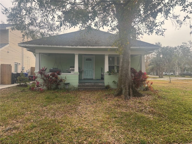 bungalow featuring a shingled roof, a front yard, and covered porch