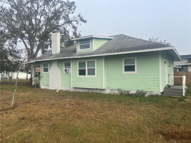 rear view of house featuring a shingled roof, cooling unit, a lawn, and a chimney