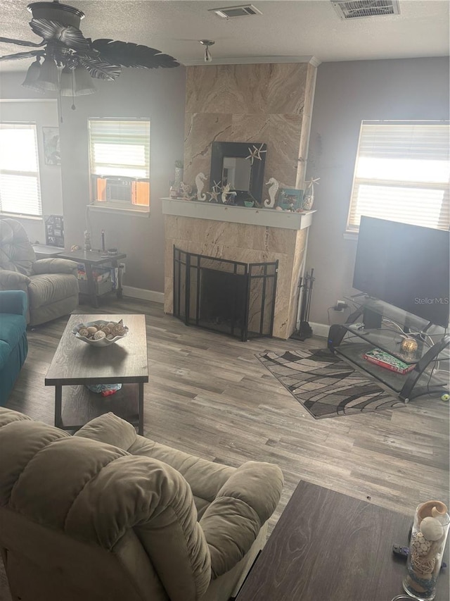 living area with a large fireplace, a textured ceiling, wood finished floors, and a wealth of natural light